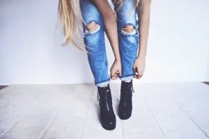 young-woman-in-ripped-jeans-putting-on-her-boots